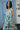 Woman wearing a floral dress standing in front of a blue door and wall with signage.