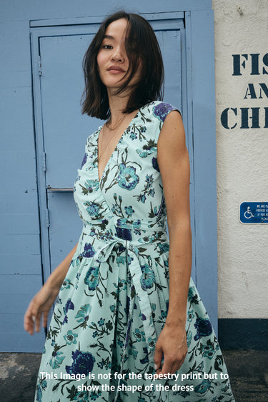 Woman wearing a floral dress standing in front of a blue door and wall with signage.