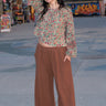 A woman standing at a beach boardwalk wearing a nutmeg brown trouser and a floral print blouse.