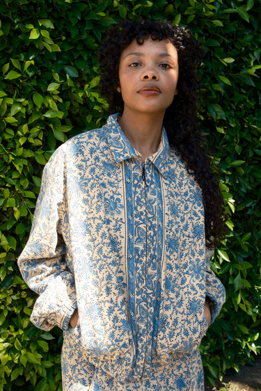 Woman wearing a blue and white patterned jacket standing against a green leafy background