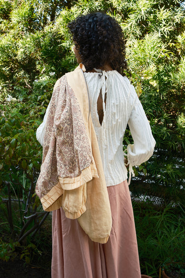 Person wearing a ivory blouse with a jacket over her shoulder showing the lining in a garden setting