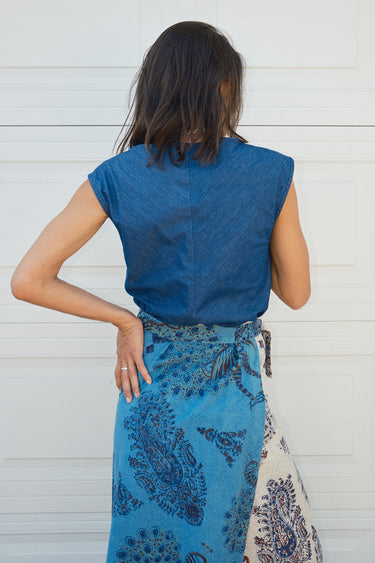 back view of woman standing in front of white wall wearing a denim top with a tapestry skirt.