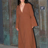 A woman standing by a metal door wearing a nutmeg brown zip front long sleeve dress.