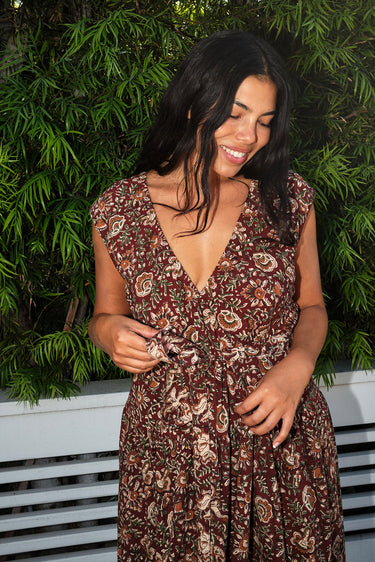 A woman wearing a raisin floral tapestry wrap dress with elastic neckline and pockets, standing outdoors.