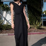 A woman standing outside wearing a long black maxi wrap dress with an empire waist and an elastic neckline.