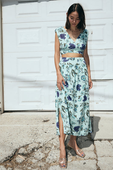 A woman wearing an aqua ground tapestry crop top and a matching skirt, standing in front of a garage white door.