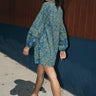  woman walking outside wearing a dark blue paisley tapestry mini dress with long sleeves. Side Back View