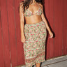 A woman wearing a floral beige ground tapestry bikini top with a matching skirt broomstick pleated standing in front of a bamboo backdrop. 