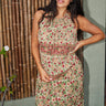 A woman wearing a floral beige ground tapestry halter top with a matching skirt broomstick pleated standing in front of a bamboo backdrop. 