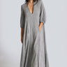 A woman standing in a white walled photo studio wearing a 3/4 sleeve maxi caftan cut from a salt and pepper textured cotton.