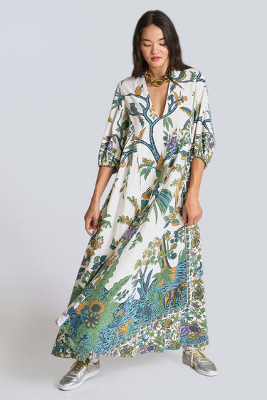 A model standing in a white photo studio wearing a maxi caftan, with three quarter balloon sleeves and  pockets. The caftan is cut from a blue and green hand block printed tree of life tapestry