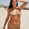 A woman at the beach wearing a beige ground, red and brown floral tapestry triangle bikini top and matching bikini bottom. 