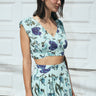 A woman wearing an aqua ground tapestry crop top and a matching skirt, standing in front of a white door.
