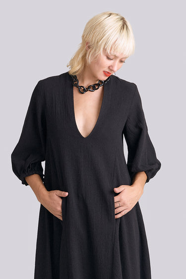 A woman standing in a white wall photo studio wearing a 3/4 sleeve midi jet black caftan.