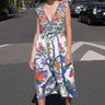 A woman standing on the sidewalk wearing a floral tapestry midi dress with an elastic neckline and pockets.
