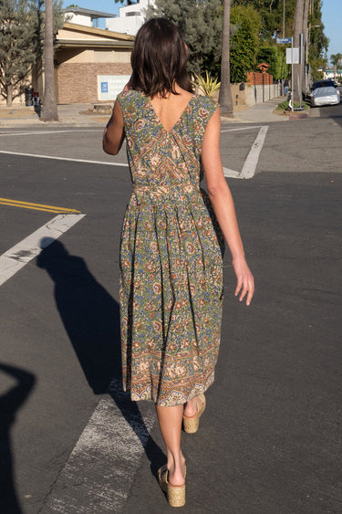 A woman standing on the sidewalk wearing a green floral tapestry midi dress with an elastic neckline and pockets.