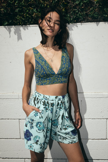 A woman standing outside wearing a dark blue paisley tapestry bra top with aqua ground floral tapestry short 