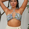 A woman wearing a white ground, lavender and blue floral tapestry bandeau bikini top and an  alabaster skirt with a tie at the waist.