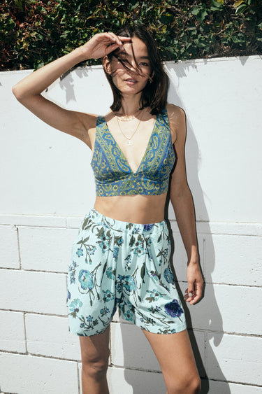 A woman standing outside wearing a dark blue paisley tapestry bra top with aqua ground floral tapestry short 