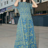 A woman at a beach boardwalk wearing a dark blue paisley tapestry maxi dress with pockets in the gathered skirt.