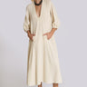 A woman standing in a white wall photo studio wearing a 3/4 sleeve midi alabaster off white caftan.
