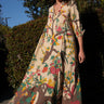 A woman standing outside by greenery wearing a maxi caftan cut in a tree of life handloom tapestry.