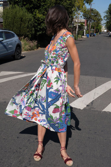 A woman standing on the sidewalk wearing a floral tapestry midi dress with an elastic neckline and pockets.