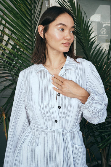 A woman outside wearing a long sleeved white with black stripe gauze shirt jacket.