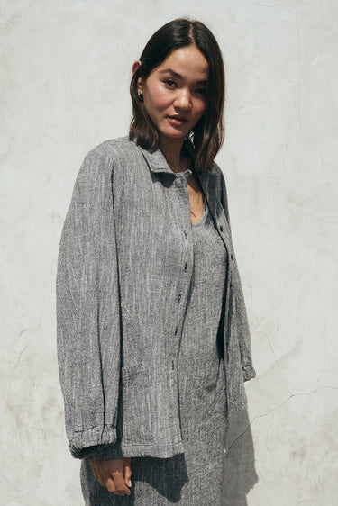 A gray unlined jacket with big patch pockets and an elastic shirred sleeve cuff, worn by a mode. She is wearing the jacket with a matching sheath dress. 