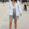 A woman wearing a white stripe jacket and bra top over gray shorts, standing on a beach pathway.