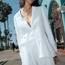 A woman standing at the beach wearing a white osnaburg shirt jacket with patch pockets and a matching trouser.