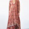 A woman in a studio with white walls wearing a red with blue flowers tapestry caftan with long sleeves. 