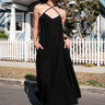 A model wearing a black circular maxi slip dress standing outside near a white picket fence with a house in the background.