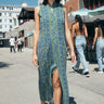 A woman  on a beach boardwalk wearing a sheath dress made from a dark blue paisley tapestry. 