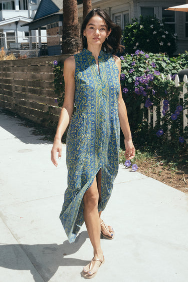 A woman  on a beach walk street wearing a sheath dress made from a dark blue paisley tapestry. 