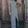 A model wearing a gray maxi shift dress with a front zipper and pockets, standing near a wooden fence.