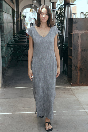 Woman standing on the side walk , outside wearing a salt and pepper yarn dye long sheath dress with a cap sleeve.  
