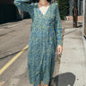A woman standing in the street wearing a long sleeve blue paisley tapestry midi wrap dress.