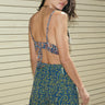 A woman standing outside wearing a blue paisley pattern  elastic waist trouser short and a bra top, back view.