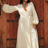 Woman standing by an ornate gate wearing a long sleeve alabaster maxi wrap dress. With a turquoise necklace.