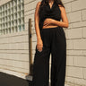 A woman standing outside next to an off white building wearing black trousers and a matching halter top.