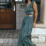 A woman wearing a blue crop top with a dark blue paisley printed design, paired with matching blue trousers, standing near a doorway.