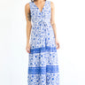 A woman standing in a studio with white walls wearing a blue and white floral tapestry maxi dress with a ruffled elastic neckline.